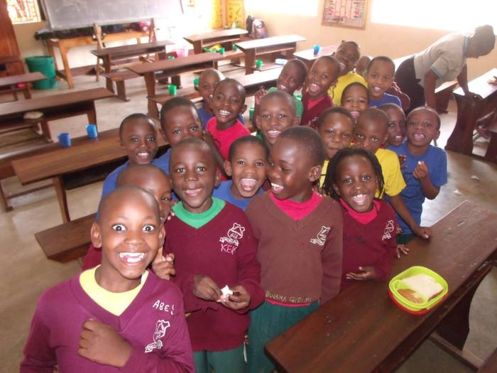 A classroom of young students in maroon uniforms smiling during a school visit
