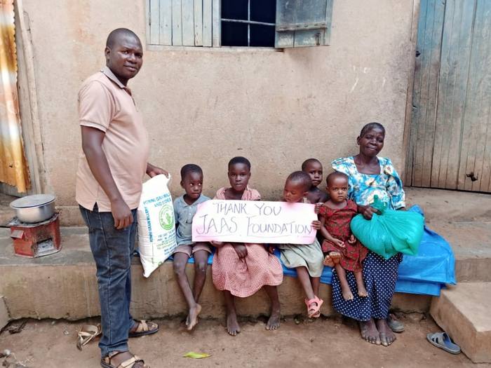 A family in Uganda with food supplies and a handwritten thank you sign for the JAAS Foundation