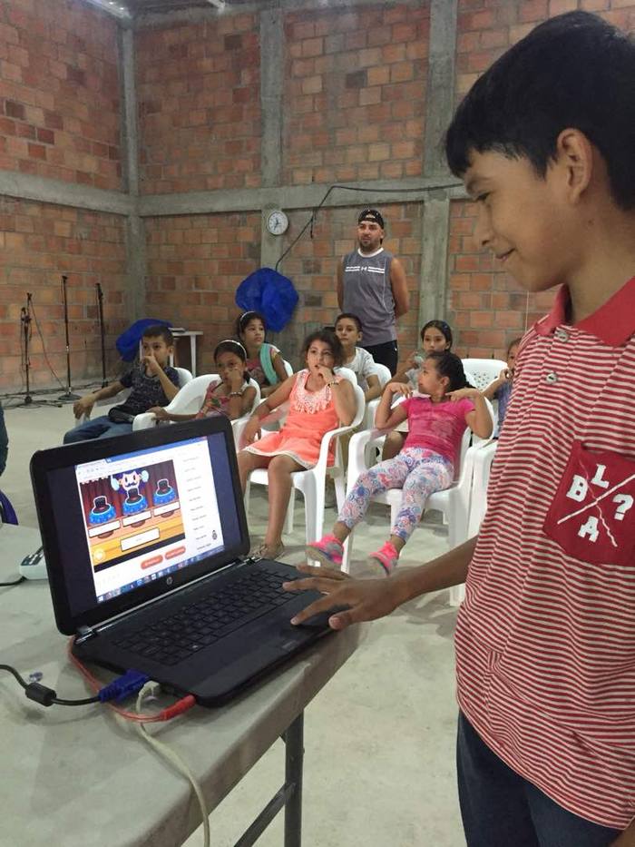 A boy presenting on a laptop to a room of children at a community learning session