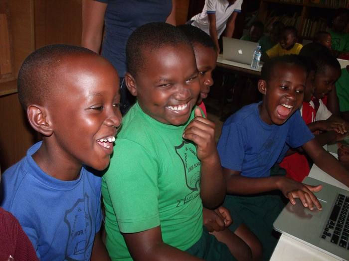 Students laughing together around donated laptops at a computer club in Uganda