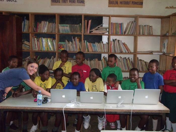 A volunteer setting up donated laptops with students in a school library in Uganda