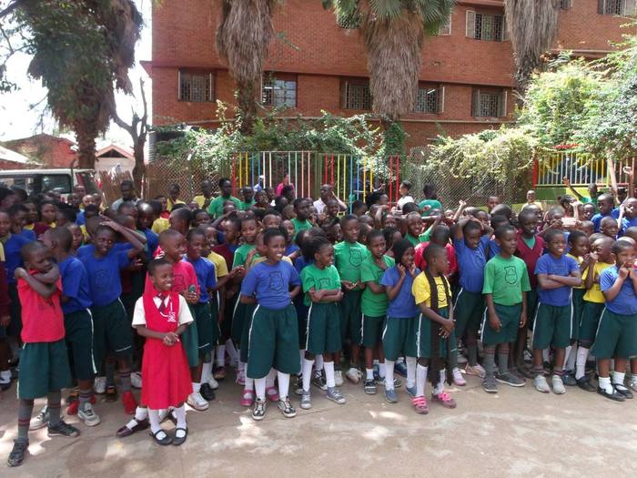 An outdoor school assembly of students in blue and green uniforms in Uganda