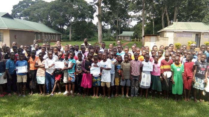 Hundreds of students gathered outdoors holding printed learning materials in Uganda