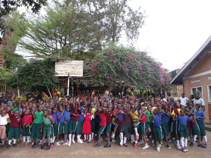 A large crowd of students waving and cheering in front of a partner school building in Uganda
